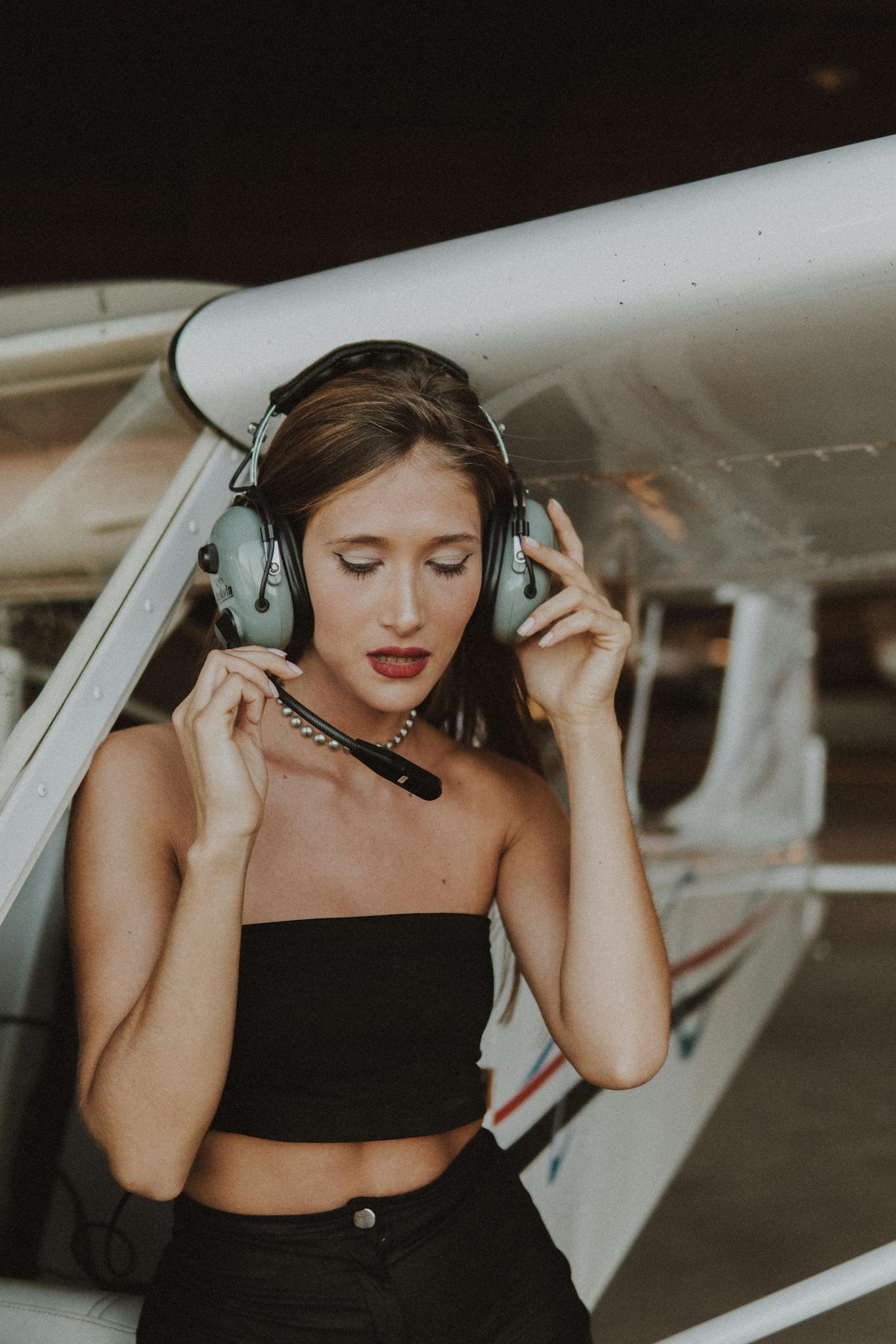Brunette woman wearing a tube top and headset near a small aircraft, exuding confidence and professionalism.