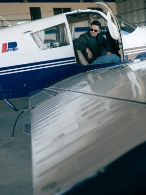 Pilot sitting in a Piper aircraft inside a hangar, ready for takeoff.